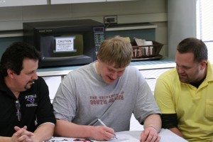 Football Coaches Gerard Rohl and John Gunderson supports Senior Bruce Manz as he signs a letter of intent to play football for University of South Dakota.  Photo by Matt Ebeling